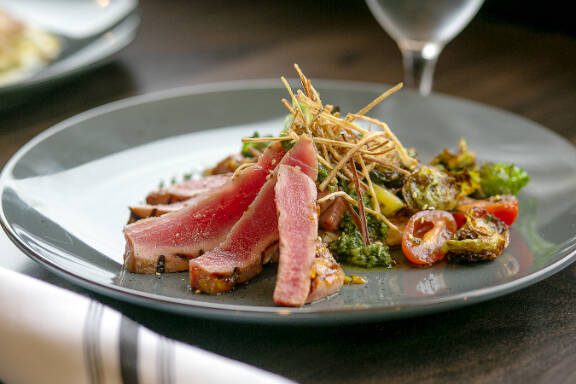 Grilled rare yellow fin tuna is served with vegetables atop a risotto cake at Hook & Cleaver on Wednesday, Nov. 1, 2023, in Mukilteo, Washington. (Ryan Berry / The Herald)