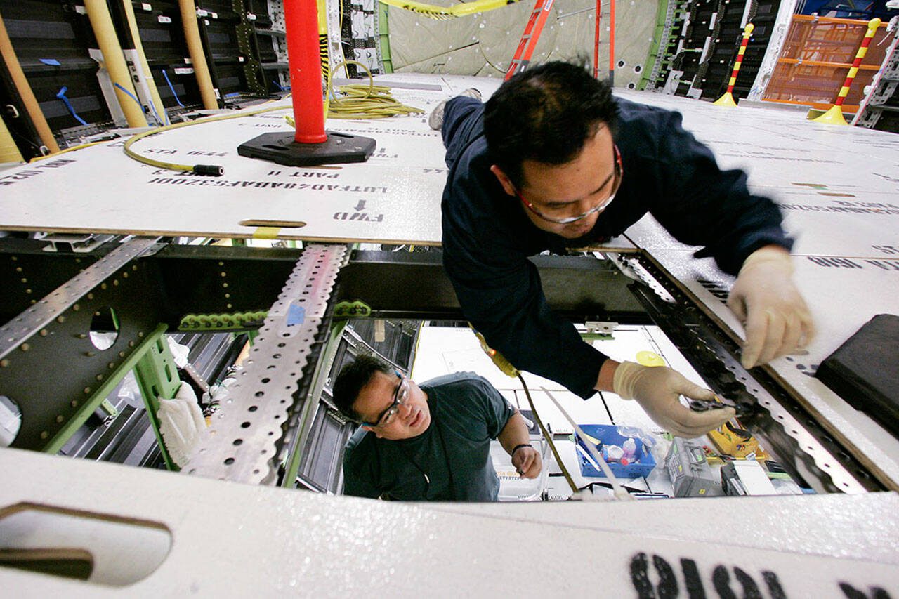 One worker looks up from the cargo area as another works in what will be the passenger compartment on one of the first Boeing 787 jets as it stands near completion at the front of the assembly line, Monday, May 19, 2008, in Everett, Washington. (AP Photo/Elaine Thompson)