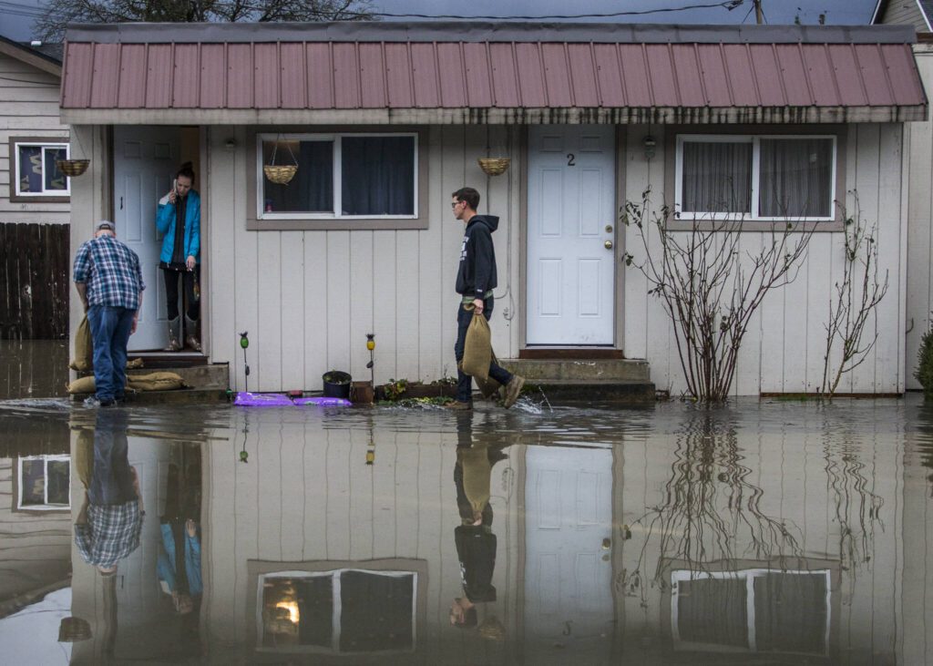 Local resident volunteers help place sandbags on the doorsteps of apartments along Main Street as river water begins to flood the street on Saturday, Feb. 1, 2020 in Sultan, Wash. (Olivia Vanni / The Herald)
