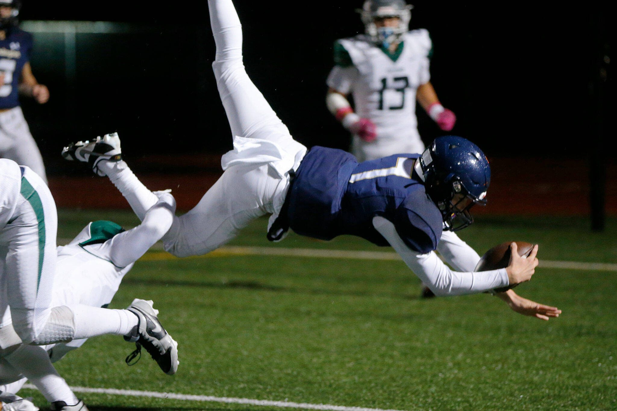 Arlington’s Leyton Martin leaps over two defenders for a rushing touchdown against Ridgeline during a playoff matchup Friday at Arlington High School in Arlington. (Ryan Berry / The Herald)