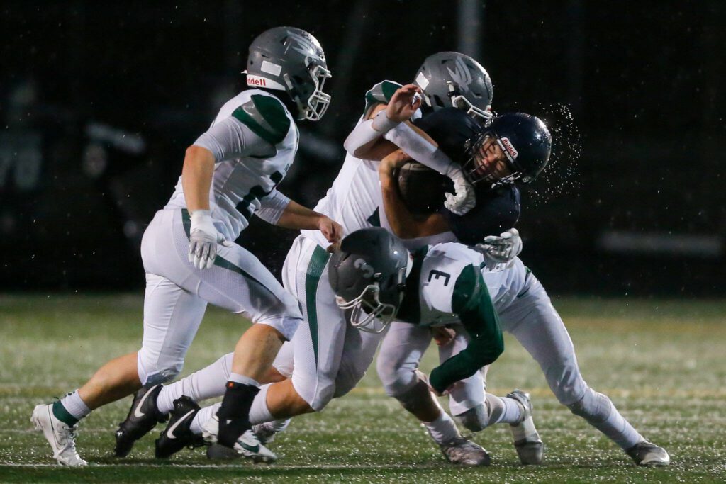 Arlington’s Caleb Reed gets hit by multiple Ridgeline defenders during a playoff matchup Friday, Nov. 10, 2023, at Arlington High School in Arlington, Washington. (Ryan Berry / The Herald)
