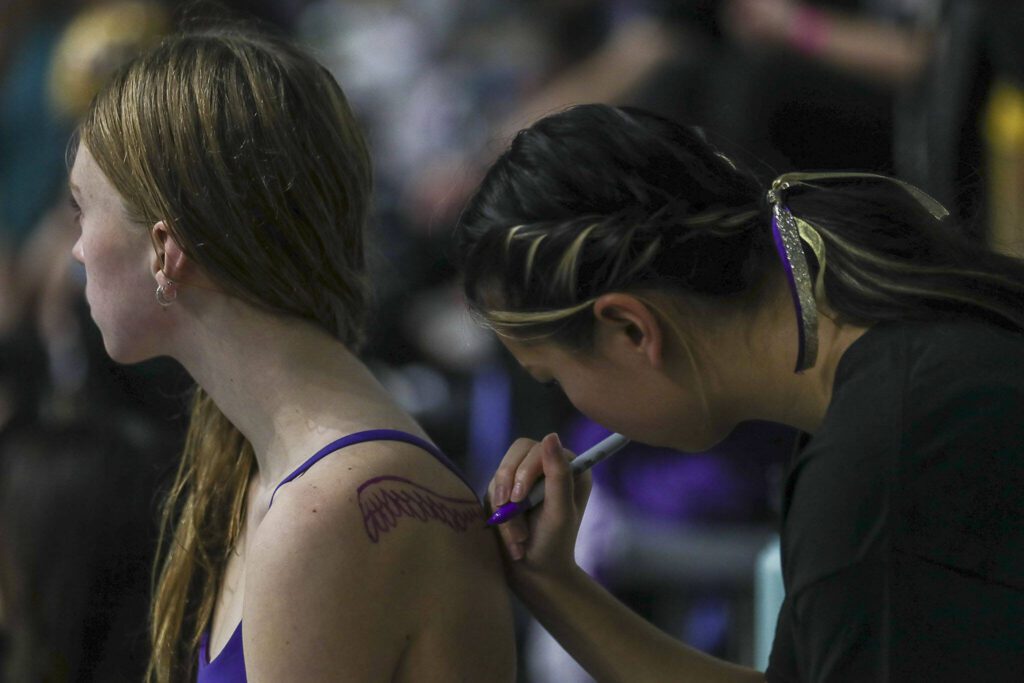 A swimmer draws wings on a fellow swimmer during the 4A girls state swim and dive championships at King County Aquatic Center in Federal Way, Washington on Saturday, Nov. 11, 2023. (Annie Barker / The Herald)
