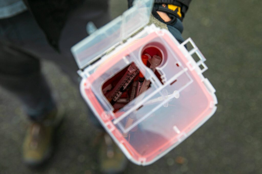Evan Reed holds a sharps container filled halfway with needles on Sunday, Nov. 19, 2023, in Everett, Washington. Reed said he has already filled one container during his cleanups and is onto his second one. (Ryan Berry / The Herald)
