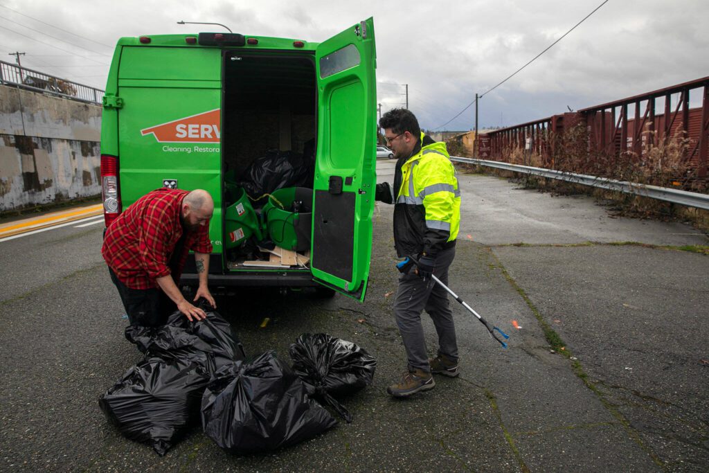 Evan Reed, right, receives help from Mike Watson loading up bags of litter collected along Marine View on Sunday, Nov. 19, 2023, in Everett, Washington. Reed, Watson and two others managed to fill ten bags of trash in two hours before taking the trash to a dumpster along the waterfront.(Ryan Berry / The Herald)
