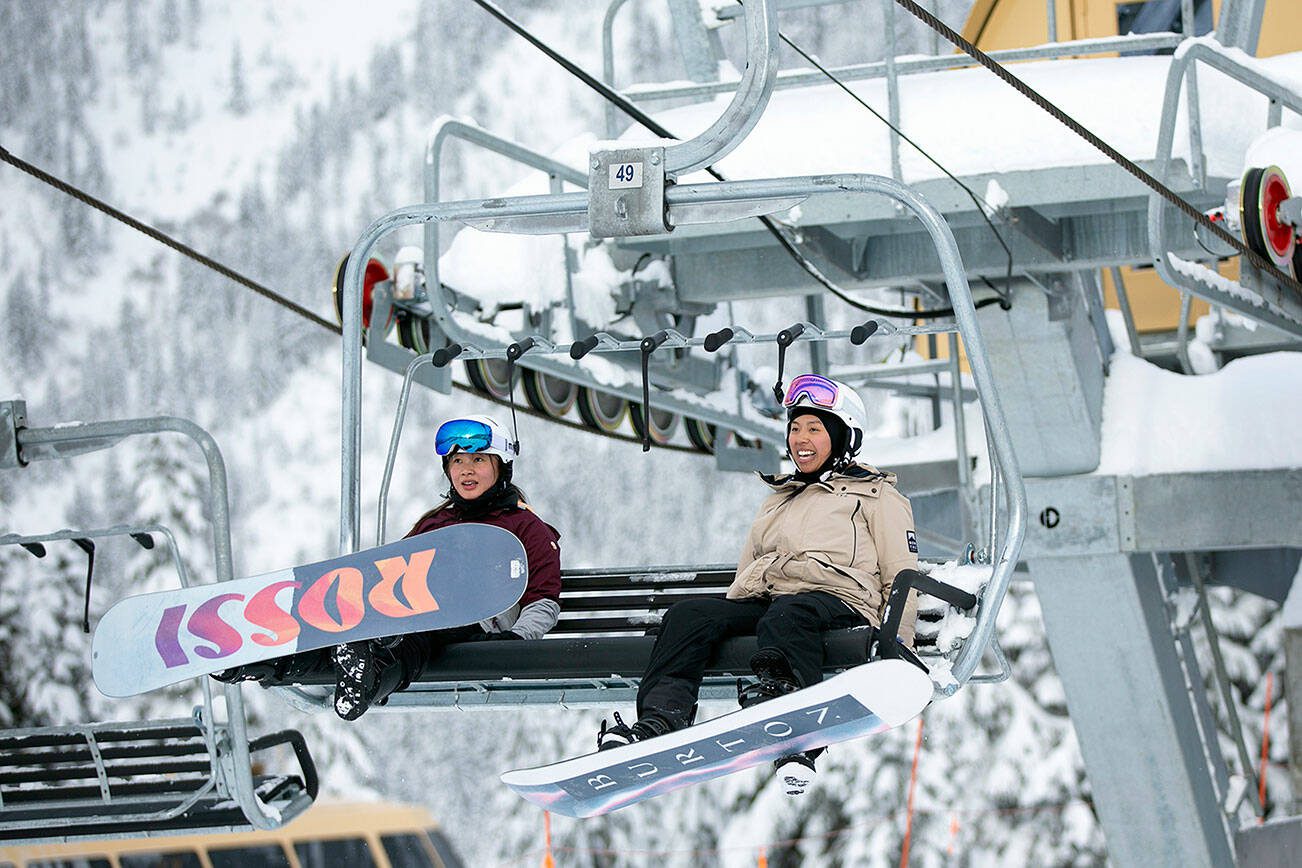 Two snowboarders head up the mountain in a lift chair on the opening day of ski season at Stevens Pass Ski Area on Friday, Dec. 2, 2022, near Skykomish, Washington. (Ryan Berry / The Herald)