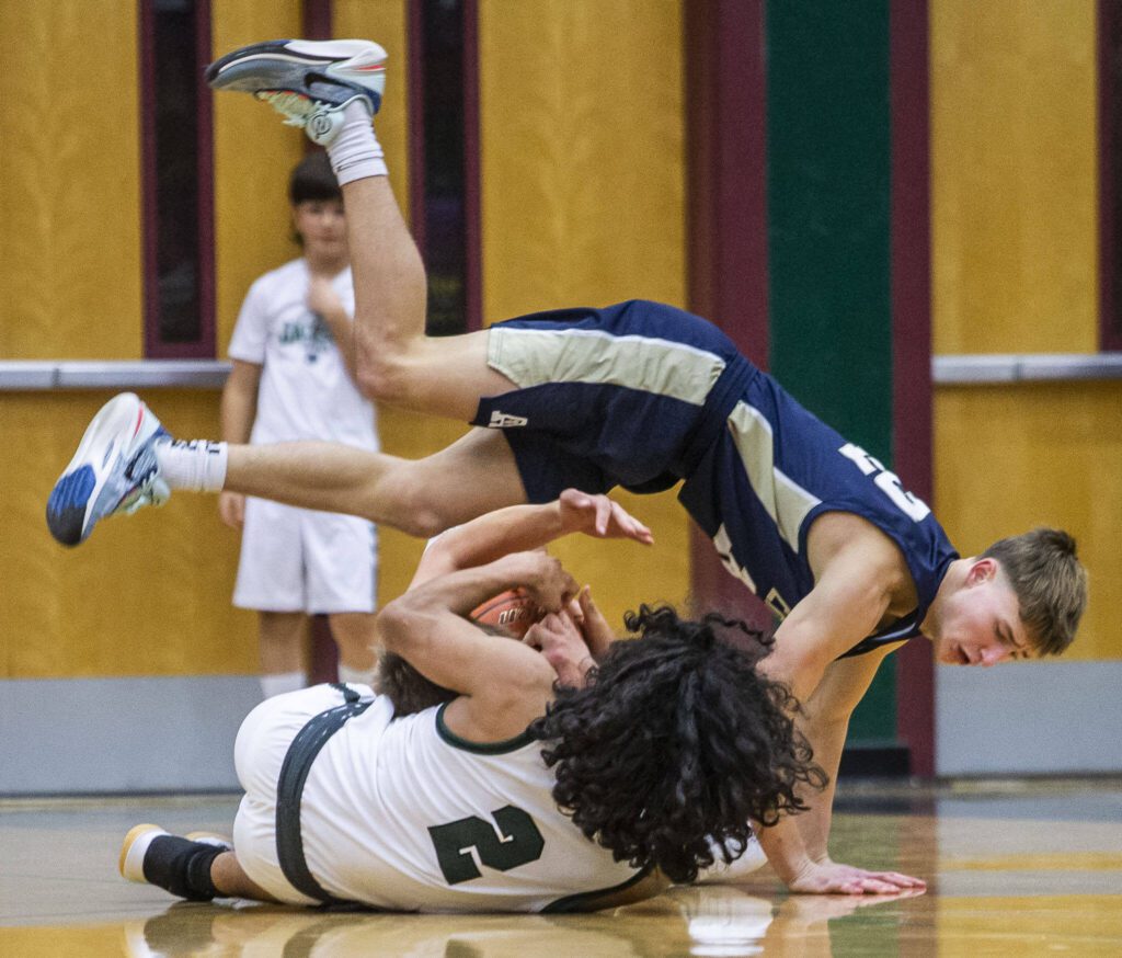 Arlington’s Kaid Hunter tumbles over Jackson’s Seamus Williams during the game on Tuesday, Nov. 28, 2023 in Everett, Washington. (Olivia Vanni / The Herald)
