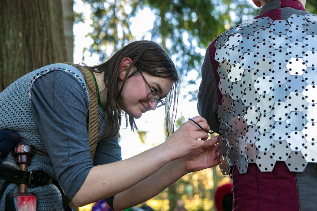 Wyvern Peters, persona Kodiak Rubus, helps another player fasten some armor prior to a “ring the bell” tournament during a weekly meeting of the Amtgard LARPing group The Hollow on Jan. 29, at McCollum Park. (Ryan Berry / The Herald)
