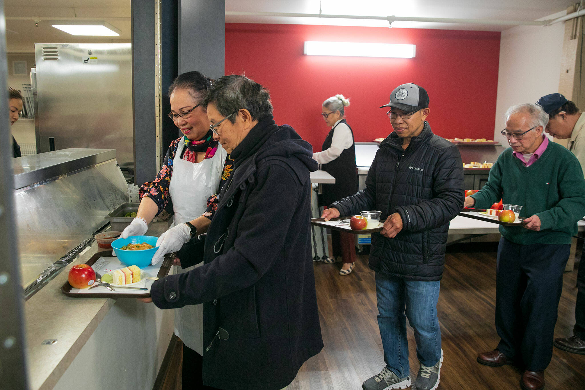 A volunteer helps distribute bowls of fried chicken noodle soup to a line of elders during a Vietnamese community lunch at the Homage Multicultural Senior Center on Wednesday, Nov. 15, 2023, in Lynnwood, Washington. (Ryan Berry / The Herald)