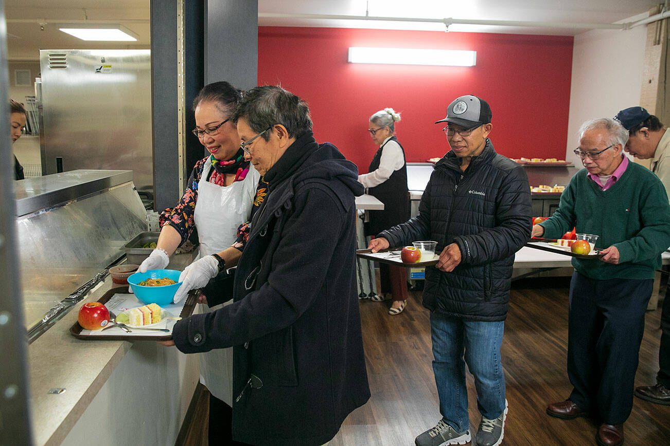 A volunteer helps distribute bowls of fried chicken noodle soup to a line of elders during a Vietnamese community lunch at the Homage Multicultural Senior Center on Wednesday, Nov. 15, 2023, in Lynnwood, Washington. (Ryan Berry / The Herald)