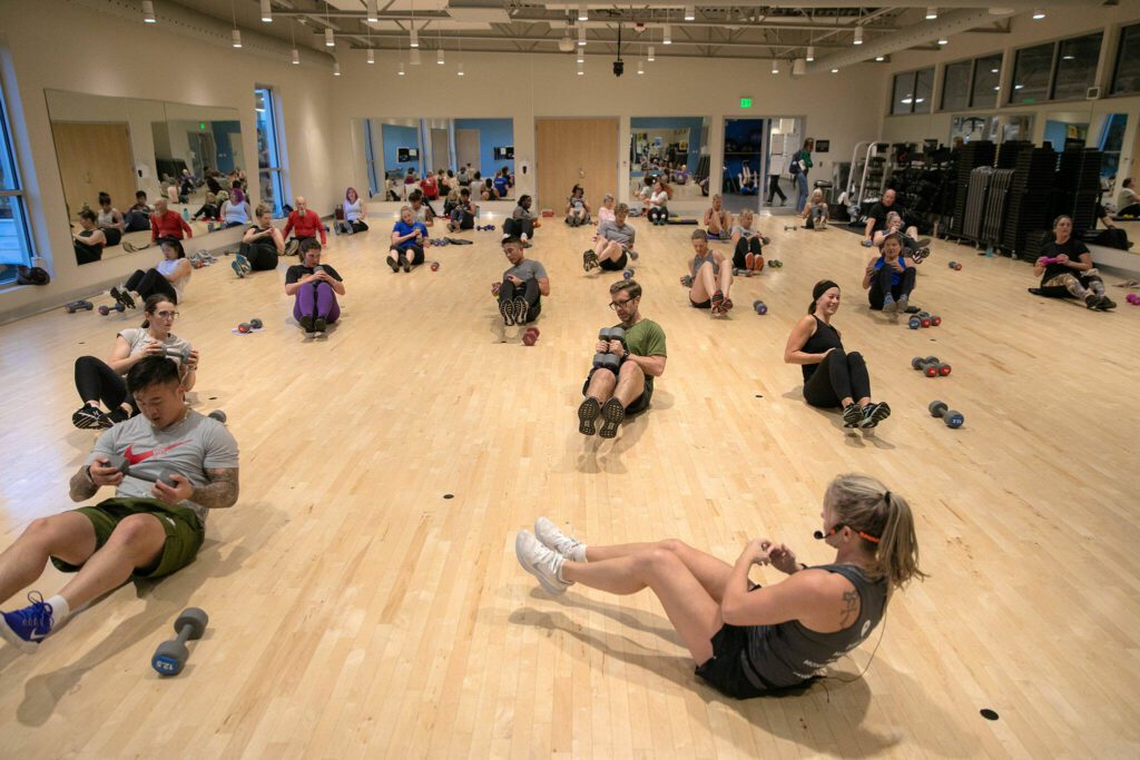Instructor Gael Gebow shows her class how to do Russian twists during her Boot Camp fitness class Monday, Nov. 13, 2023, at the YMCA in Everett, Washington. (Ryan Berry / The Herald)
