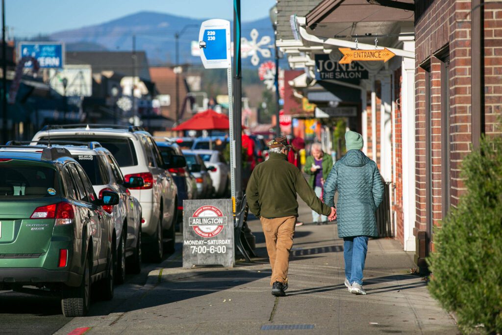 A couple walks up North Olympic Avenue on Saturday, Dec. 16, 2023, in downtown Arlington, Washington. (Ryan Berry / The Herald)
