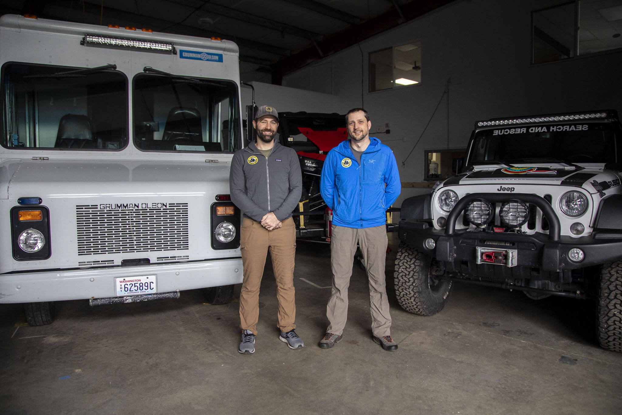 Field members Donnie Pingrey, left, and Jay Bublitz, right, pose for a photo in front of vehicles at the Everett Mountain Rescue headquarters in Snohomish, Washington on Thursday, Nov. 16, 2023. (Annie Barker / The Herald)