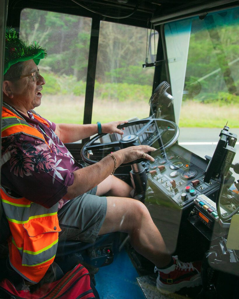 Island Transit driver Tino Gutierrez, a Navy veteran who has been a transit driver for two decades, laughs while talking about his route on Tuesday, Dec. 19, 2023, somewhere outside Oak Harbor, Washington. Gutierrez wears festive getup for holidays year-round as a way to brighten his own life and the life of others. (Ryan Berry / The Herald)

