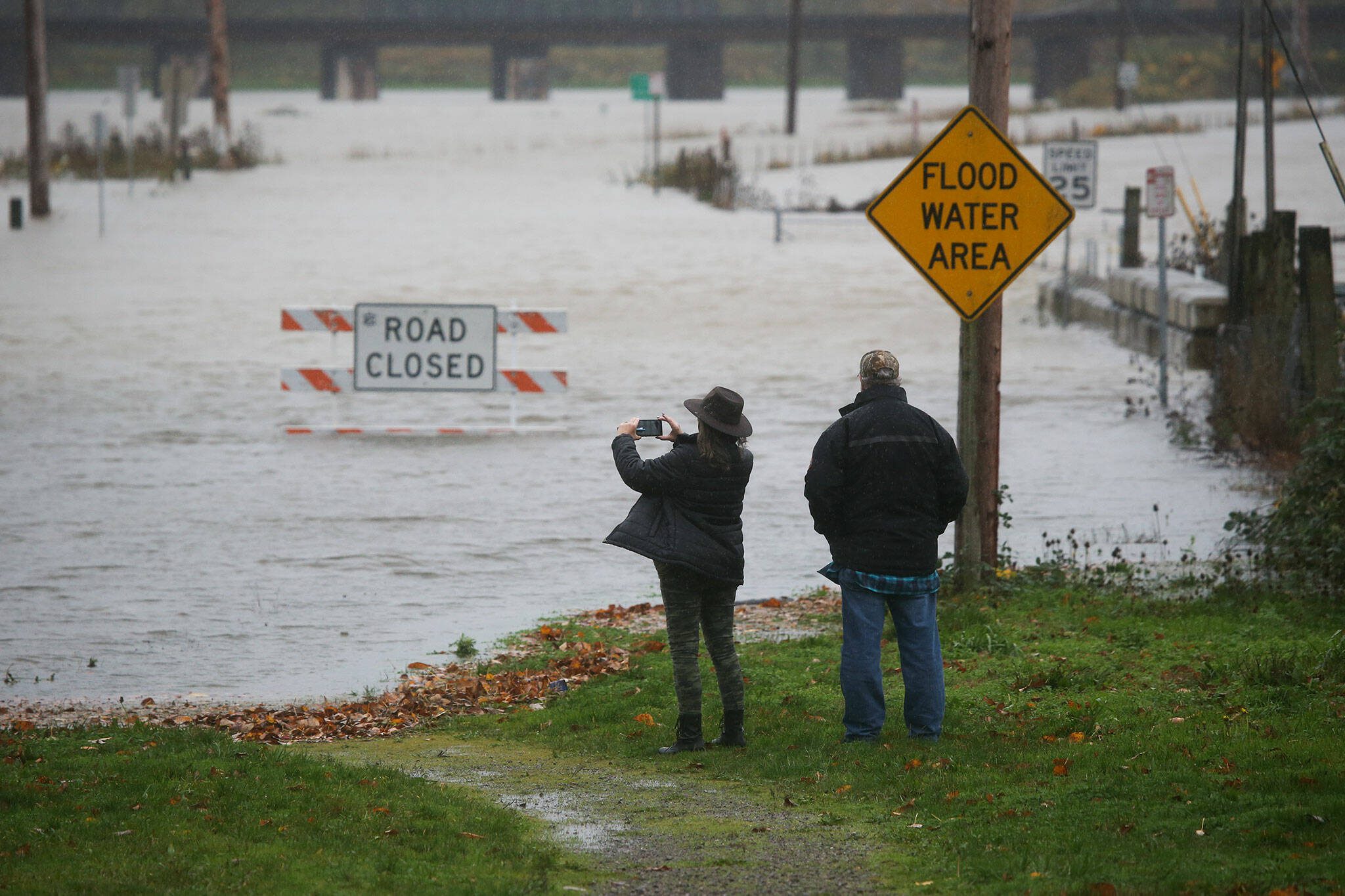 Pam and Ken Owens, of Granite Falls, stop to take cell phone photos of the flooding along Lincoln Avenue on Monday, Nov. 15, 2021 in Snohomish, Washington. The couple were planing to take the road to Monroe for lunch. (Andy Bronson / The Herald)