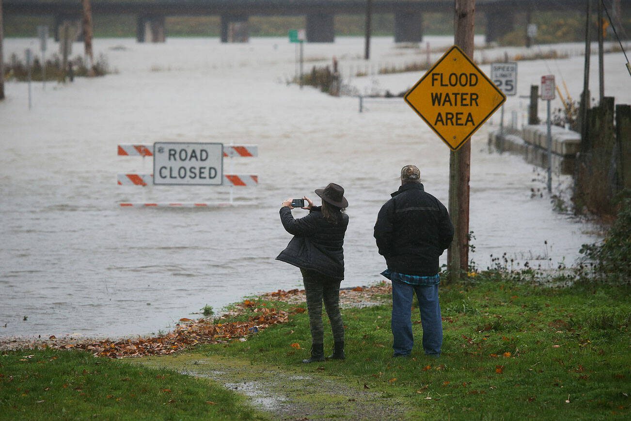 Pam and Ken Owens, of Granite Falls,  stop to take cell phone photos of the flooding along Lincoln Avenue on Monday, Nov. 15, 2021 in Snohomish, Washington. The couple were planing to take the road to Monroe for lunch.   (Andy Bronson / The Herald)