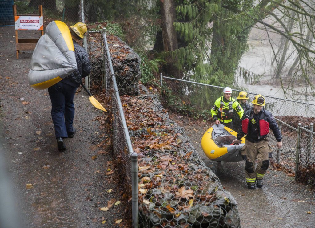 Snohomish Regional Fire & Rescue members carry their inflatable rescue boat up Al Borlin Park Trail on Tuesday, Dec. 5, 2023 in Monroe, Washington. (Olivia Vanni / The Herald)

