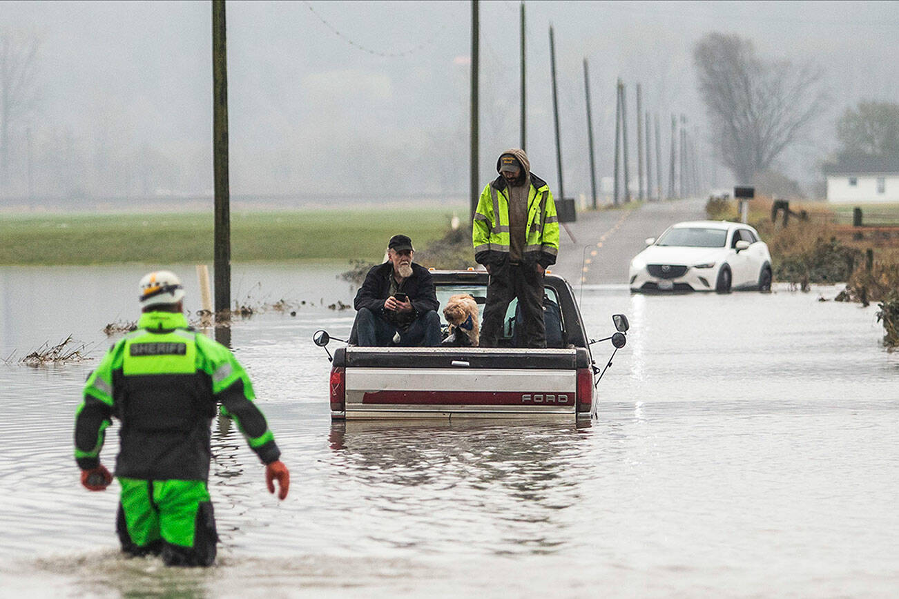 Snohomish County Sheriff Dive Team and Search and Rescue deputy William Dawson approach two men and two dogs sitting in the bed of their truck. The truck died while trying to cross floodwaters along 28th Avenue NW on Wednesday, Dec. 6, 2023, in Stanwood, Washington. (Olivia Vanni / The Herald)