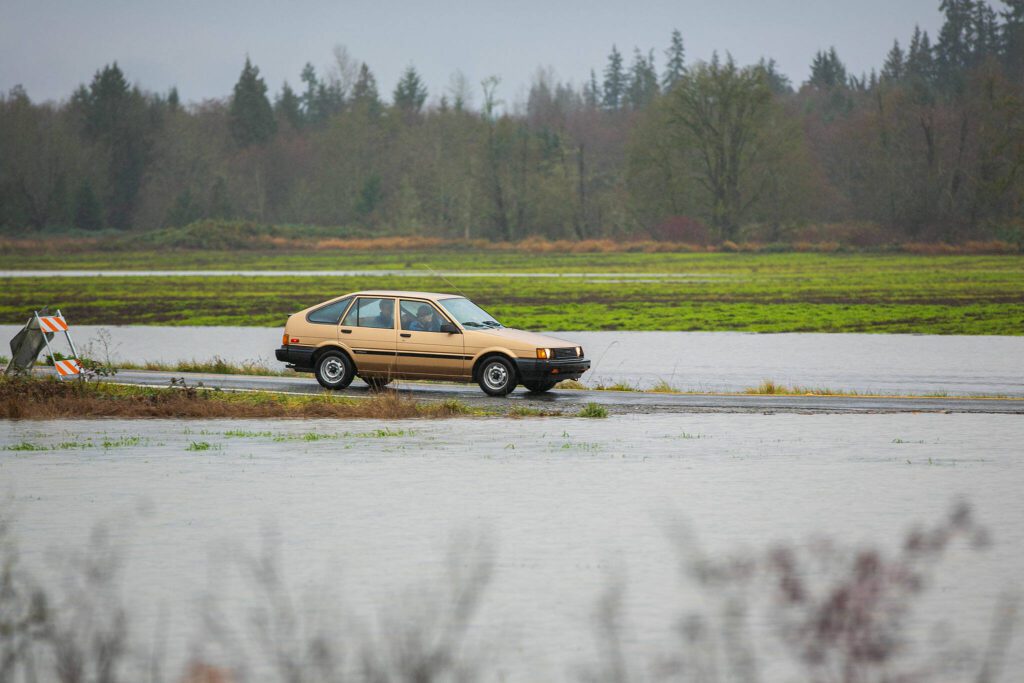 A vehicle turns onto 212th Street NE and crosses over a small amount of water on Thursday, Dec. 7, 2023, after extensive flooding from the Stillaguamish River in Silvana, Washington. (Ryan Berry / The Herald)
