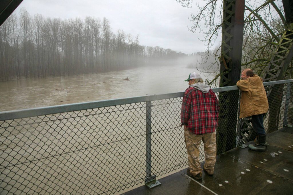 Two men look out over the confluence of the North and South forks of the Stillaguamish River from atop Haller Bridge during heavy flooding on Tuesday, Dec. 5, 2023, in Arlington, Washington. People from all over the area came to the bridge to get a look at the river. (Ryan Berry / The Herald)
