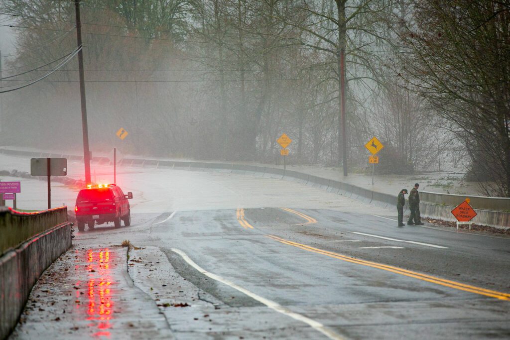A group of park rangers have a look at the flood waters along the Stillaguamish on Highway 530 after closing down Twin Rivers Park during heavy flooding on Tuesday, Dec. 5, 2023, in Arlington, Washington. (Ryan Berry / The Herald)
