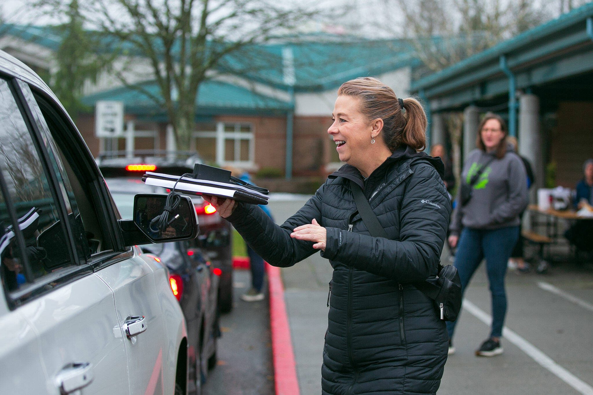 Assistant Superintendent Patty Dowd greets a family with their child’s laptop and other class materials outside Endeavour Elementary on Wednesday, Dec. 6, 2023, two days after an overnight fire tore through the inside of the school in Mukilteo, Washington. Classes will be held online until after winter break to give crews time to make repairs to the building. (Ryan Berry / The Herald)