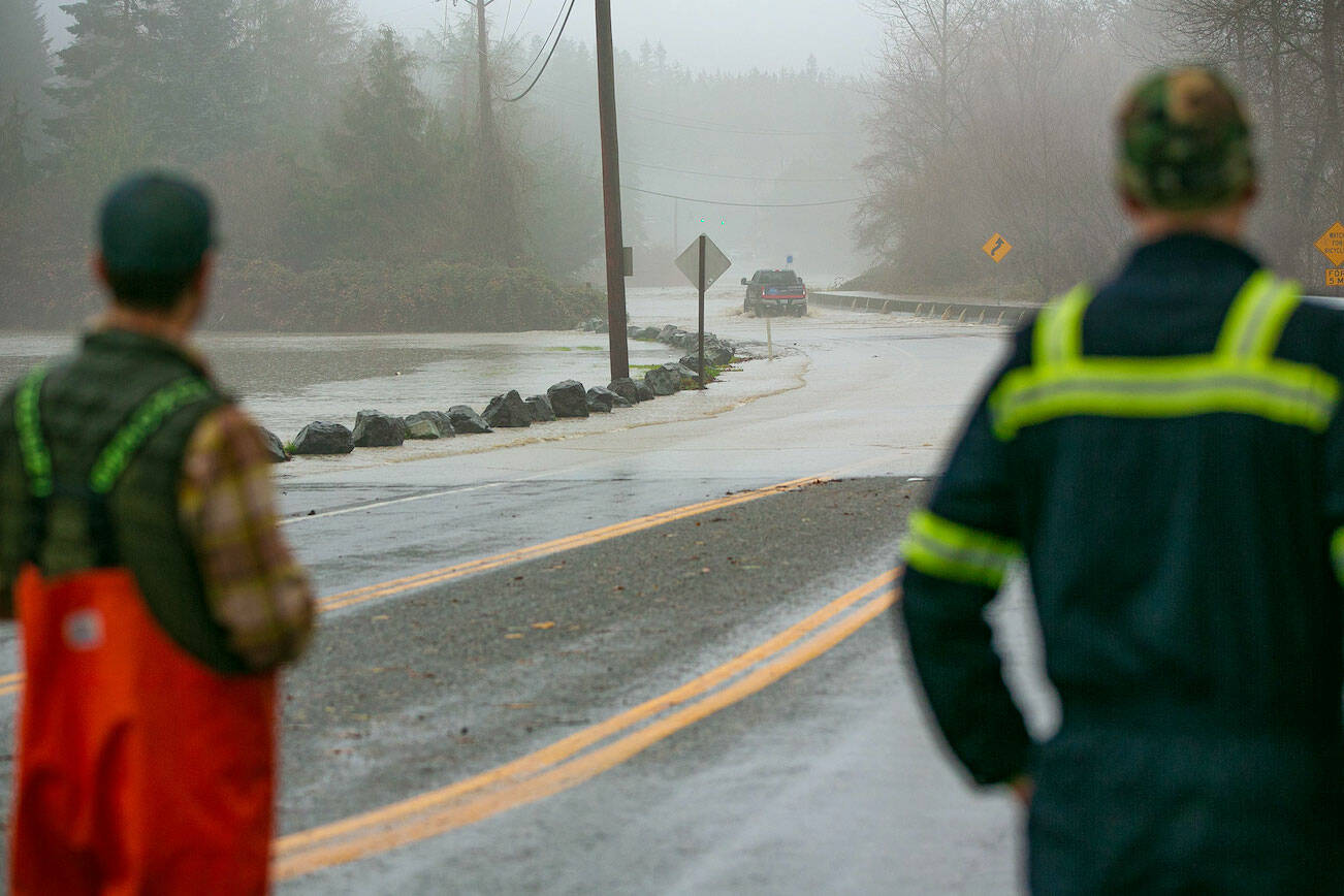 Two drivers watch as a person in a lifted Ford fords a flooded Route 530 near Twin Rivers Park during heavy flooding on Tuesday, Dec. 5, 2023, in Arlington, Washington. (Ryan Berry / The Herald)