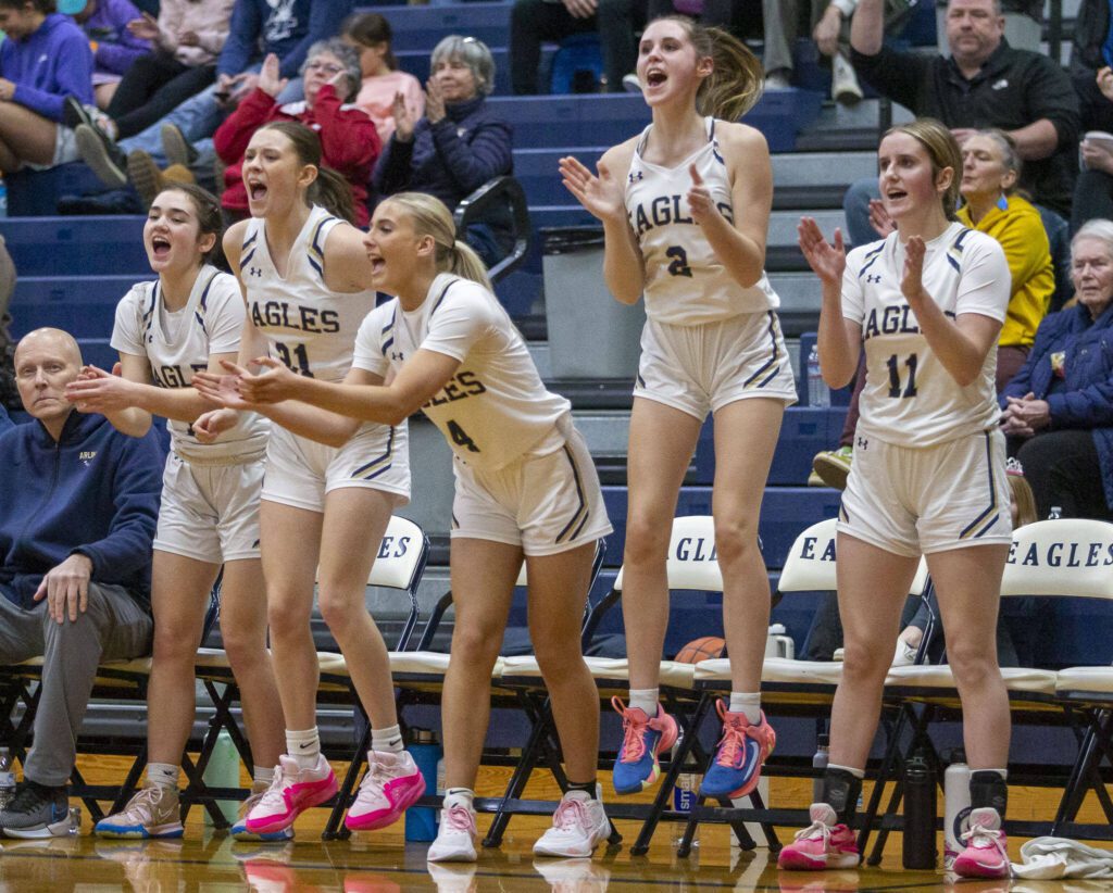 The Arlington bench reacts to teammate Samara Morrow making a three-point shot during the game against Lynnwood on Monday, Dec. 11, 2023 in Arlington, Washington. (Olivia Vanni / The Herald)
