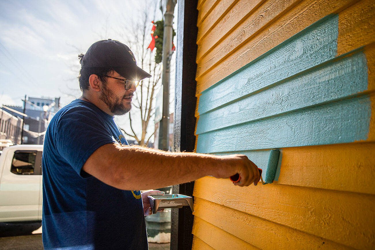 Evan Reed helps repaint the yellow exterior of the Catalyst Cafe along Hewitt Avenue on Thursday, Dec. 21, 2023 in Everett, Washington. (Olivia Vanni / The Herald)