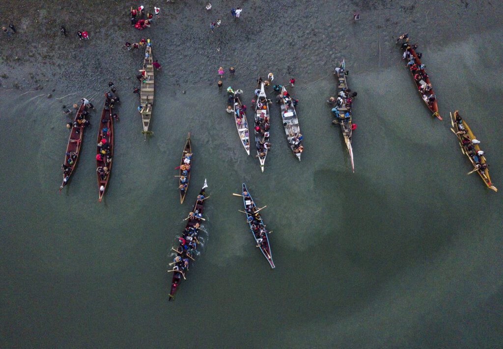 Dozens of colorful canoes are maneuvered into the water of Tulalip Bay as canoe families began another day of their journey to Muckleshoot on Friday, July 28, 2023 in Tulalip, Washington. (Olivia Vanni / The Herald)
