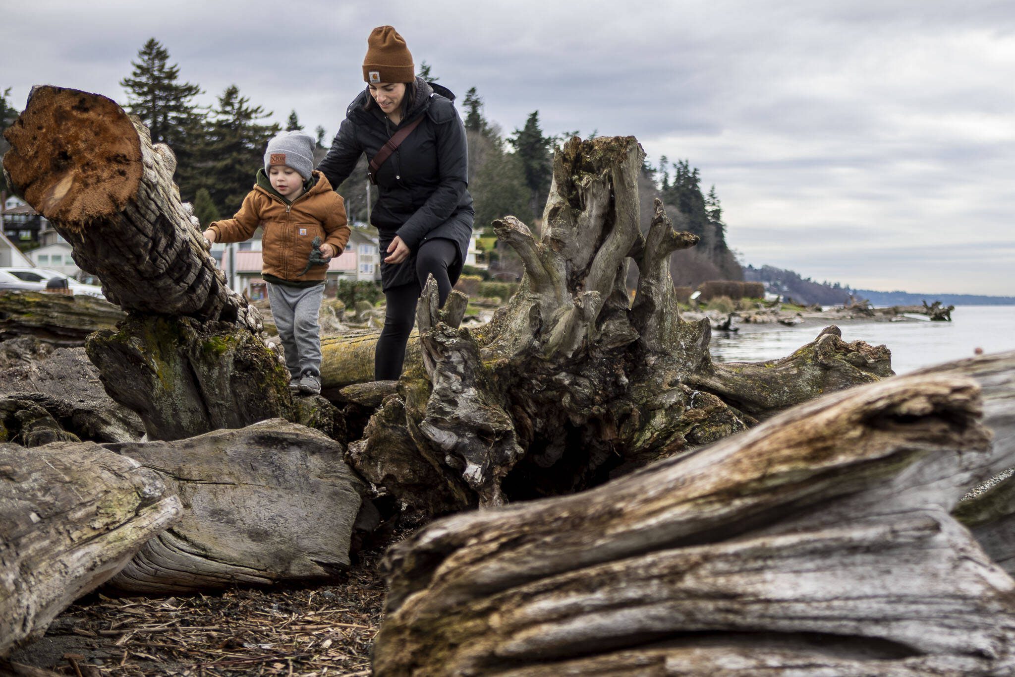 Boone Bisbey, 2, and Hunnika Bisbey, 39, walk along the beach and driftwood at Lighthouse Park in Mukilteo, Washington, on Wednesday, Jan. 3, 2024. (Annie Barker / The Herald)