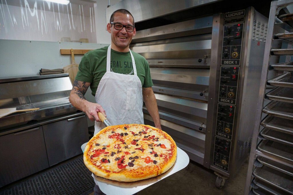 Paul Sarkis presents a finished pizza. He and his wife Lila Sarkis recently started a take-and-bake pizza business. (Photo by David Welton)
