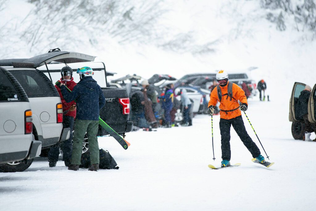 A man skis through the parking lot on his way to the mountain on the opening day of ski season at Stevens Pass Ski Area on Friday, Dec. 2, 2022, near Skykomish, Washington. (Ryan Berry / The Herald) 
