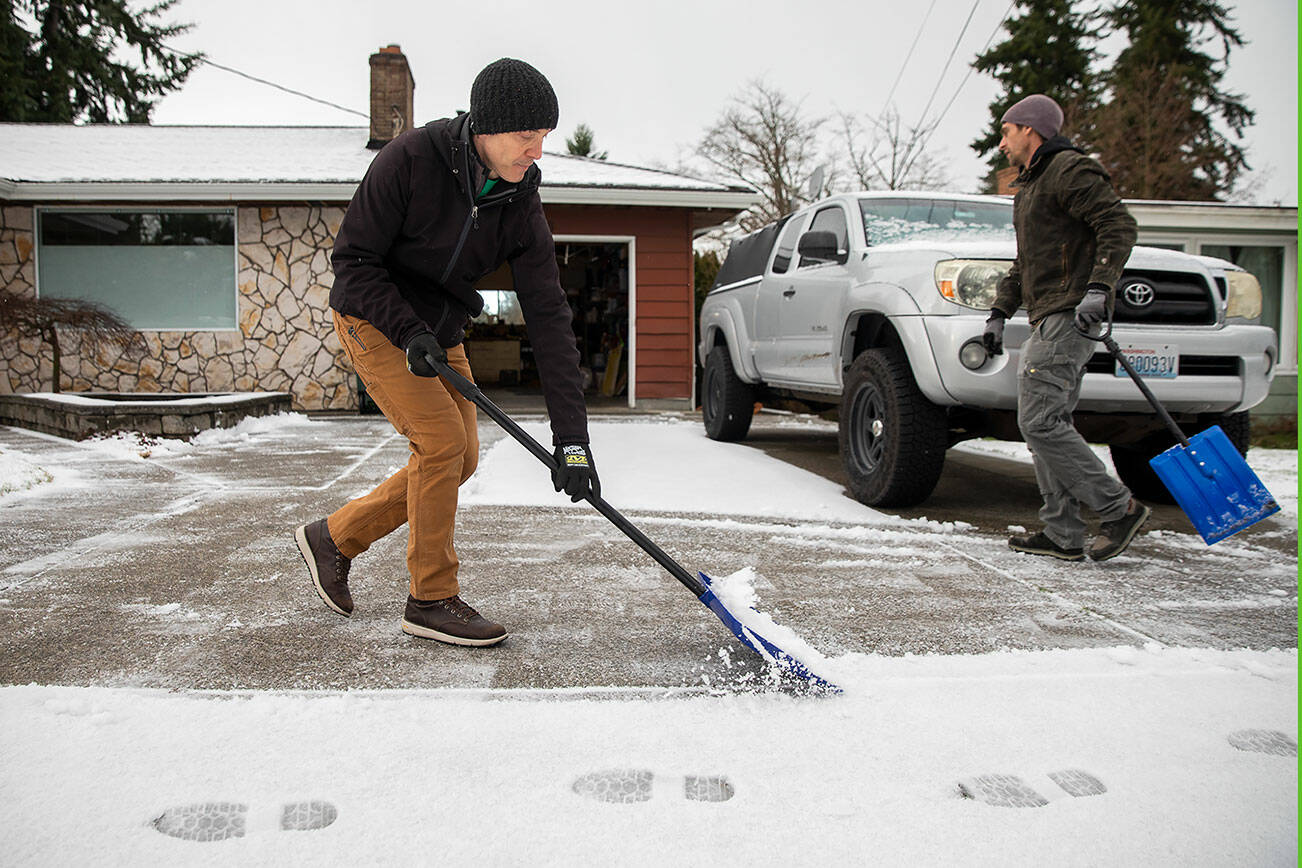 Shanti Curran, left, and Andy McKee, right, shovel Curran’s driveway after a light dusting of snow fell on Thursday morning in Everett, Washington. Curran said he normally wouldn’t shovel with such a small amount of snow but the looming below freezing temperatures over the next few days have him worried about potential ice. (Olivia Vanni / The Herald)