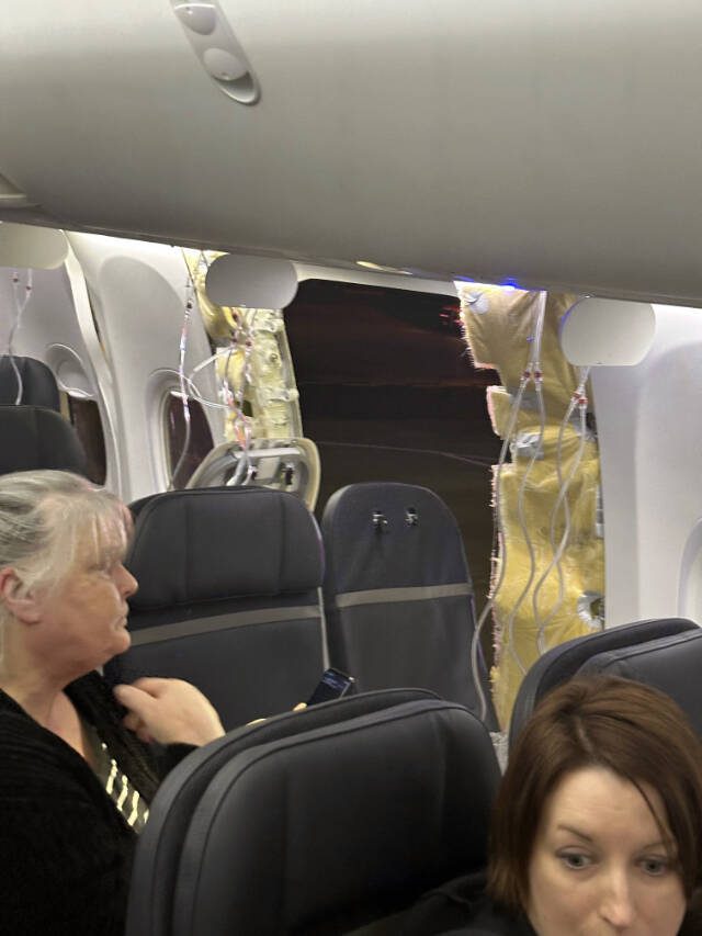This image provided by passenger Kelly Bartlett shows other passengers near a hole in the fuselage of an Alaska Airlines Boeing 737 Max 9, Flight 1282, which was forced to return to Portland International Airport on Jan. 5. (Kelly Bartlett via AP)
