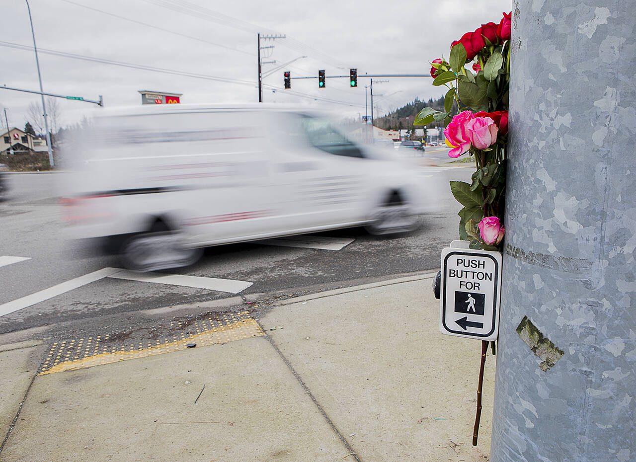 A car drives by flowers placed at a memorial for two pedestrians killed at the corner of 204th Street NE and Highway 9 on Friday, Jan. 21, 2022 in Arlington, Washington. (Olivia Vanni / The Herald)