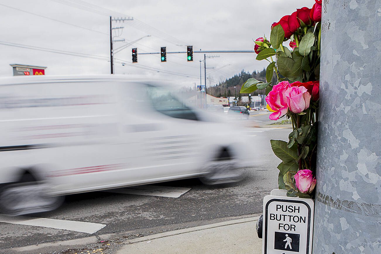 A car drives by flowers placed at a memorial for two pedestrians killed at the corner of 204th Street NE and Highway 9 on Friday, Jan. 21, 2022 in Arlington, Washington. (Olivia Vanni / The Herald)