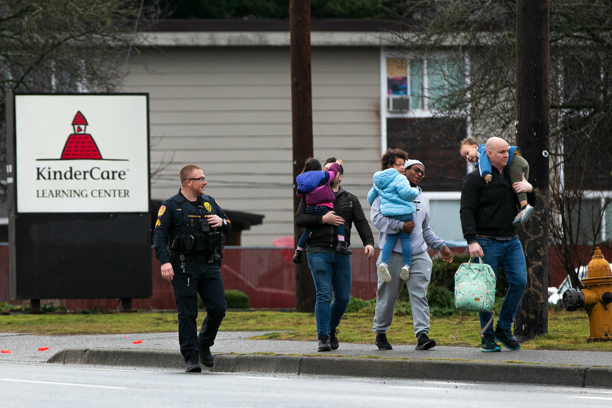 An officer escorts three parents with their children away from KinderCare after a shooting across the street at the Bluffs at Evergreen apartment complex Monday, Jan. 22, 2024, in Everett, Washington. Parents were able to get their children from the daycare center during the standoff. (Ryan Berry / The Herald)