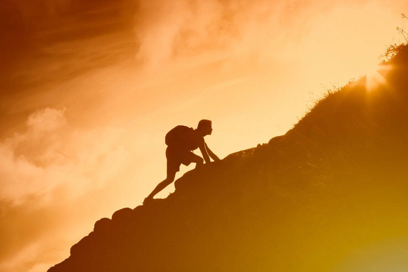 Silhouette of man climbing up a mountain