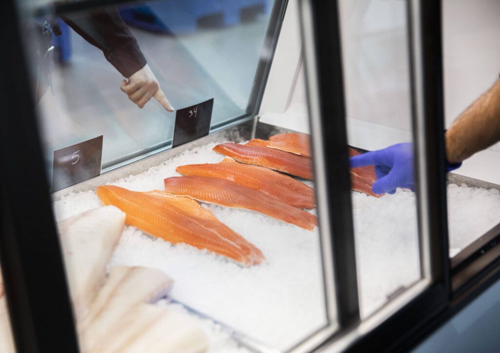 A customer selects a salmon fillet. The shop sells only fish that’s been kept whole until just before it’s sold. (Olivia Vanni / The Herald)
