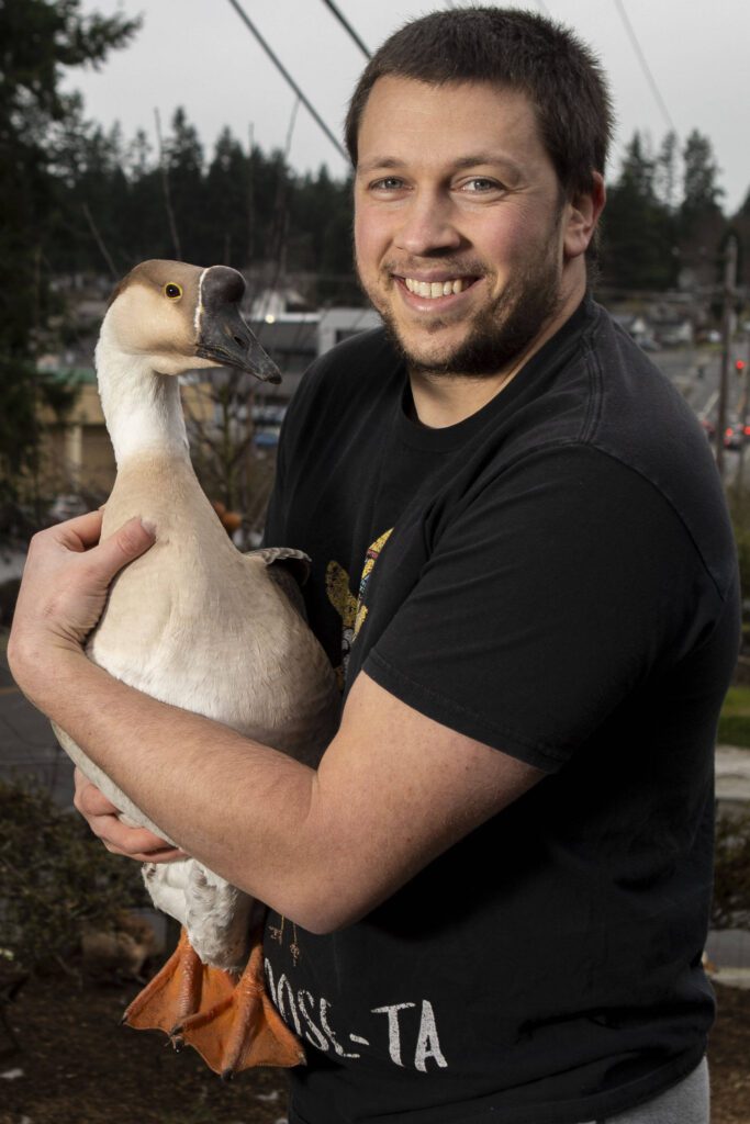 Ryan Carlson, 31, and his goose Henrietta pose for a photo outside his home in Everett. (Annie Barker / The Herald)

