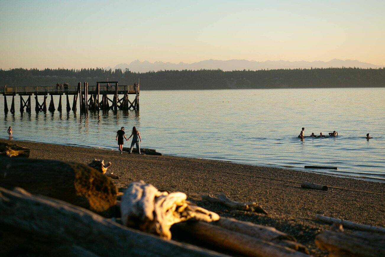 People fish from the pier, hold hands on the beach and steer a swamped canoe in the water as the sun sets on another day at Kayak Point on Monday, June 12, 2023, in Stanwood, Washington. (Ryan Berry / The Herald)