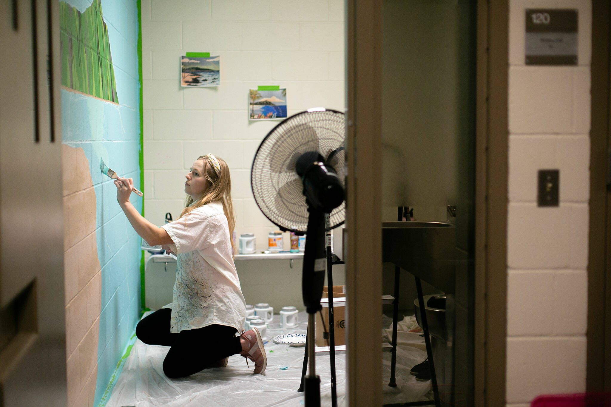 Penny Leslie works on a tropical mural inside one of the jail cells at the Mukilteo Police Station. (Ryan Berry / The Herald)