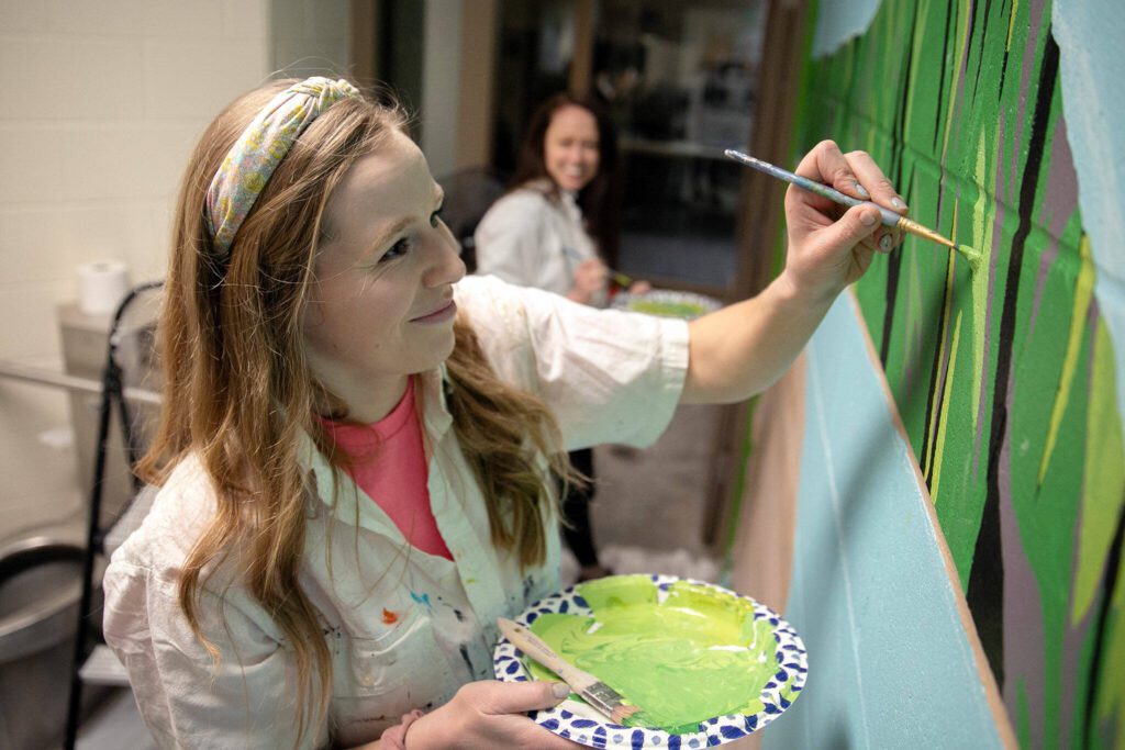 Penny Leslie, with help from her cousin Lindsey Baker, works on a mural inside one of two jail cells at the Mukilteo Police Station. (Ryan Berry / The Herald)
