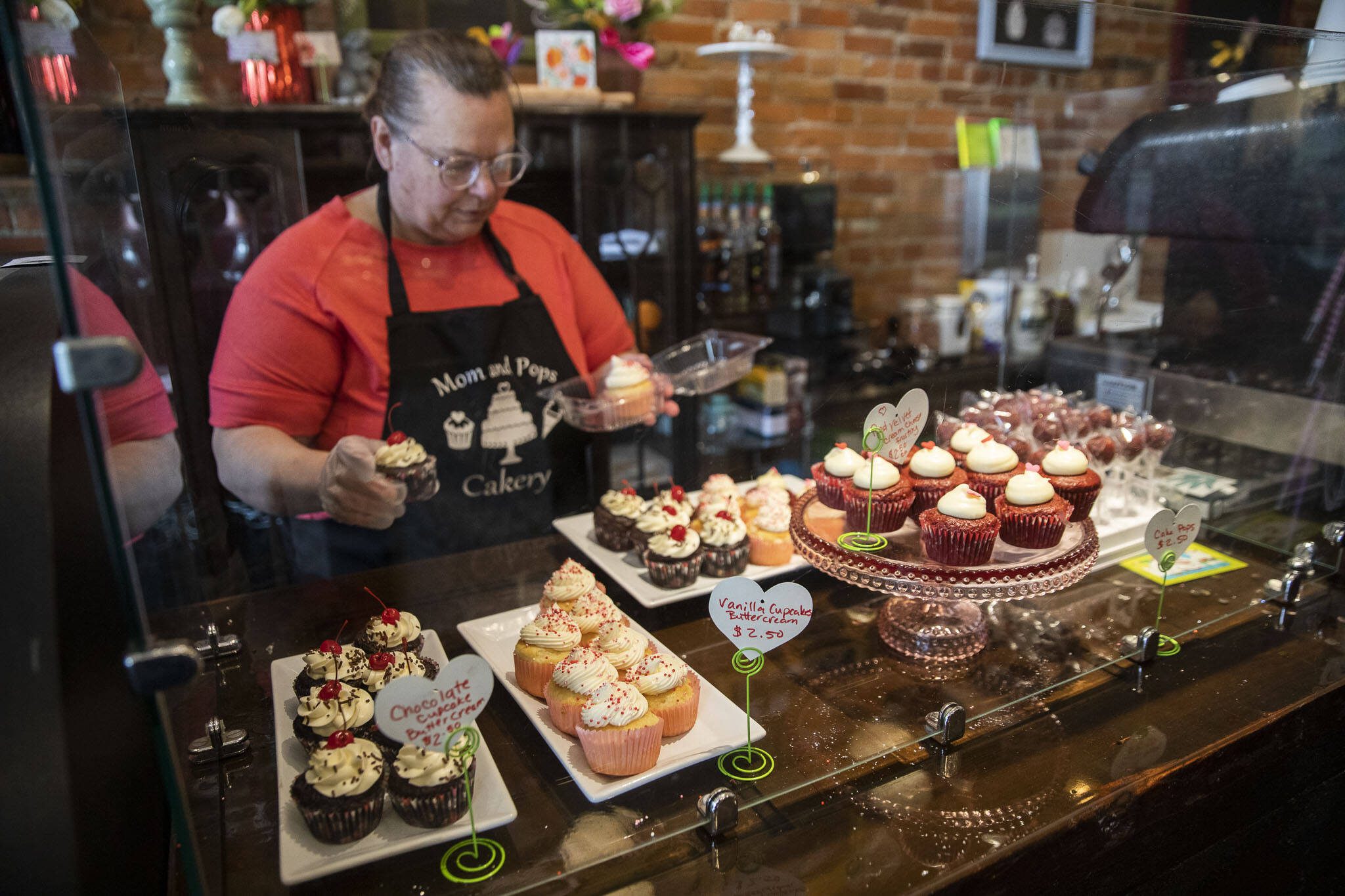 Mom and Pops Cakery owner Colleen Dunn picks out a Valentine’s Day-themed cupcake for a customer on Wednesday, Feb. 14, 2024 in Everett, Washington. (Olivia Vanni / The Herald)