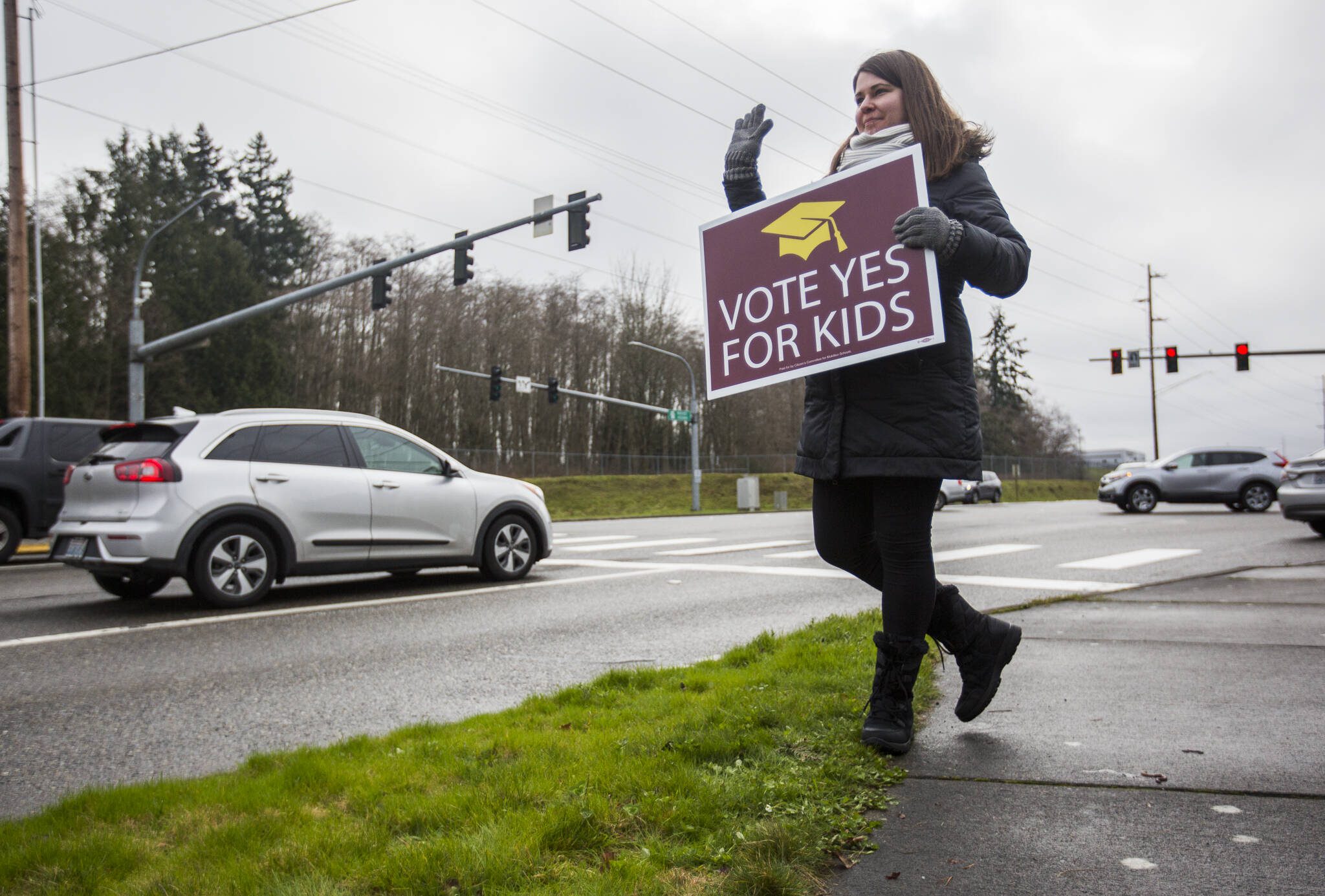 Jaime Benedict, who works as a substitute teacher, waves to drivers on the corner of Mukilteo Speedway and Harbor Pointe Boulevard while holding a sign in support of a bond proposal for Mukilteo School District in February 2020 in Mukilteo. (Olivia Vanni / The Herald file photo)