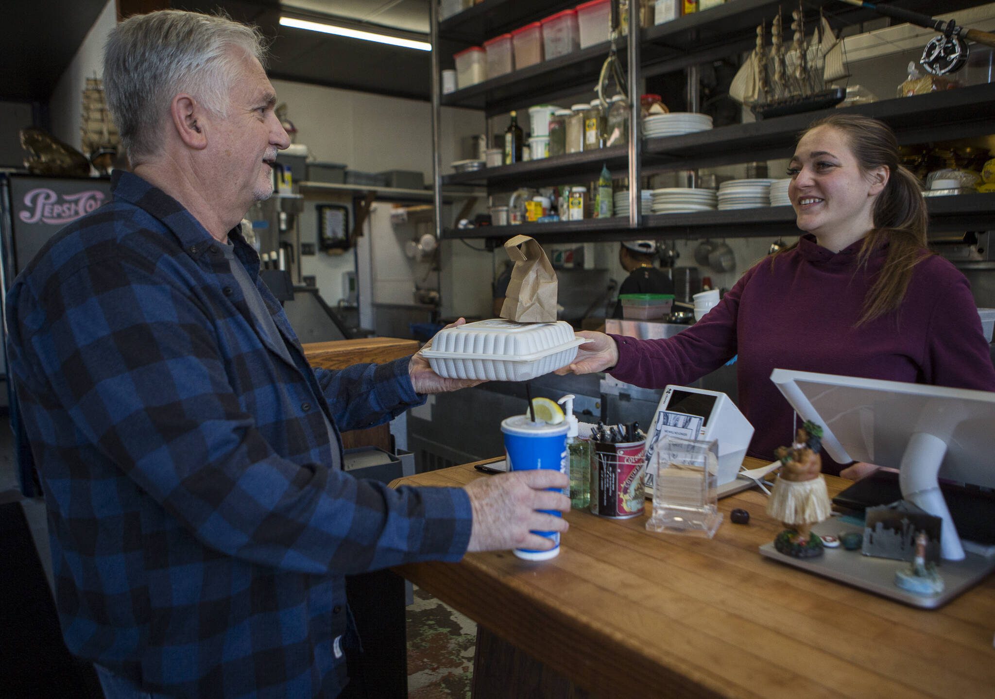 Andy’s Fish House employee Kate Gordon, right, hands Andy Coleman his to-go order on Thursday, March 19, 2020 in Snohomish, Wa. (Olivia Vanni / The Herald)