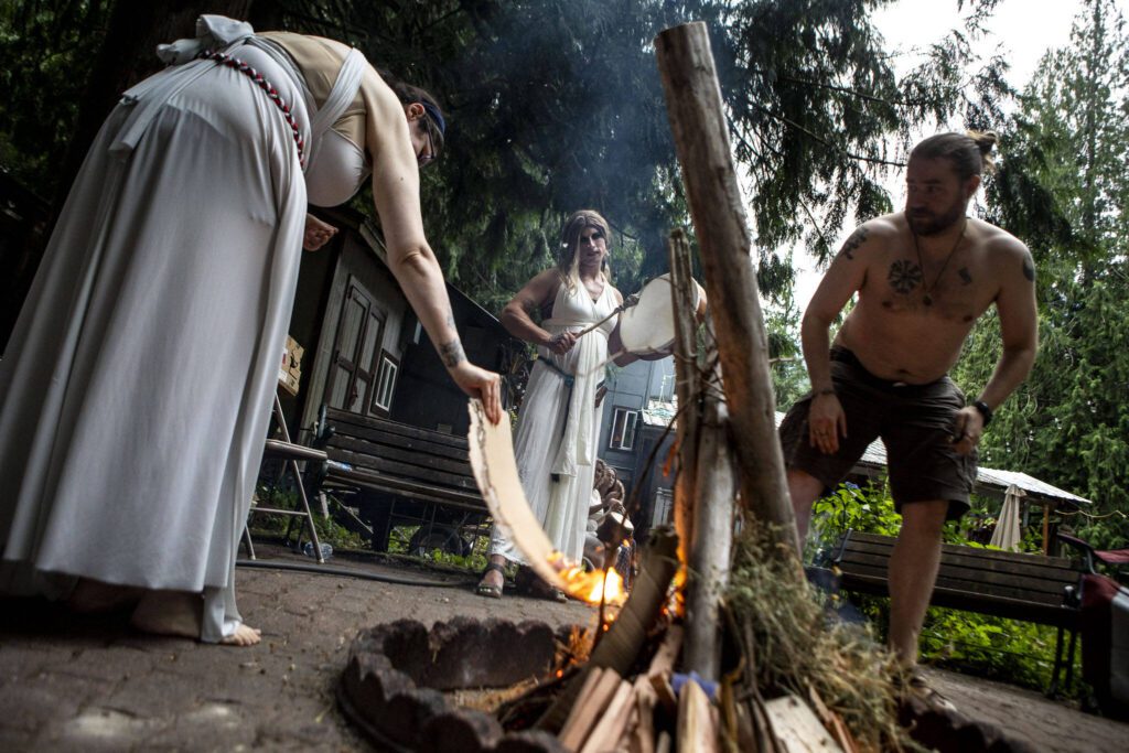 N’Mier LaVeau, left, and Jesse Sterland, right, start a fire for the Lammas and Wicker Man ritual while Mydnyte Windham, center, drums at the Aquarian Tabernacle Church in Index, Washington, in August 2023. (Annie Barker / The Herald)
