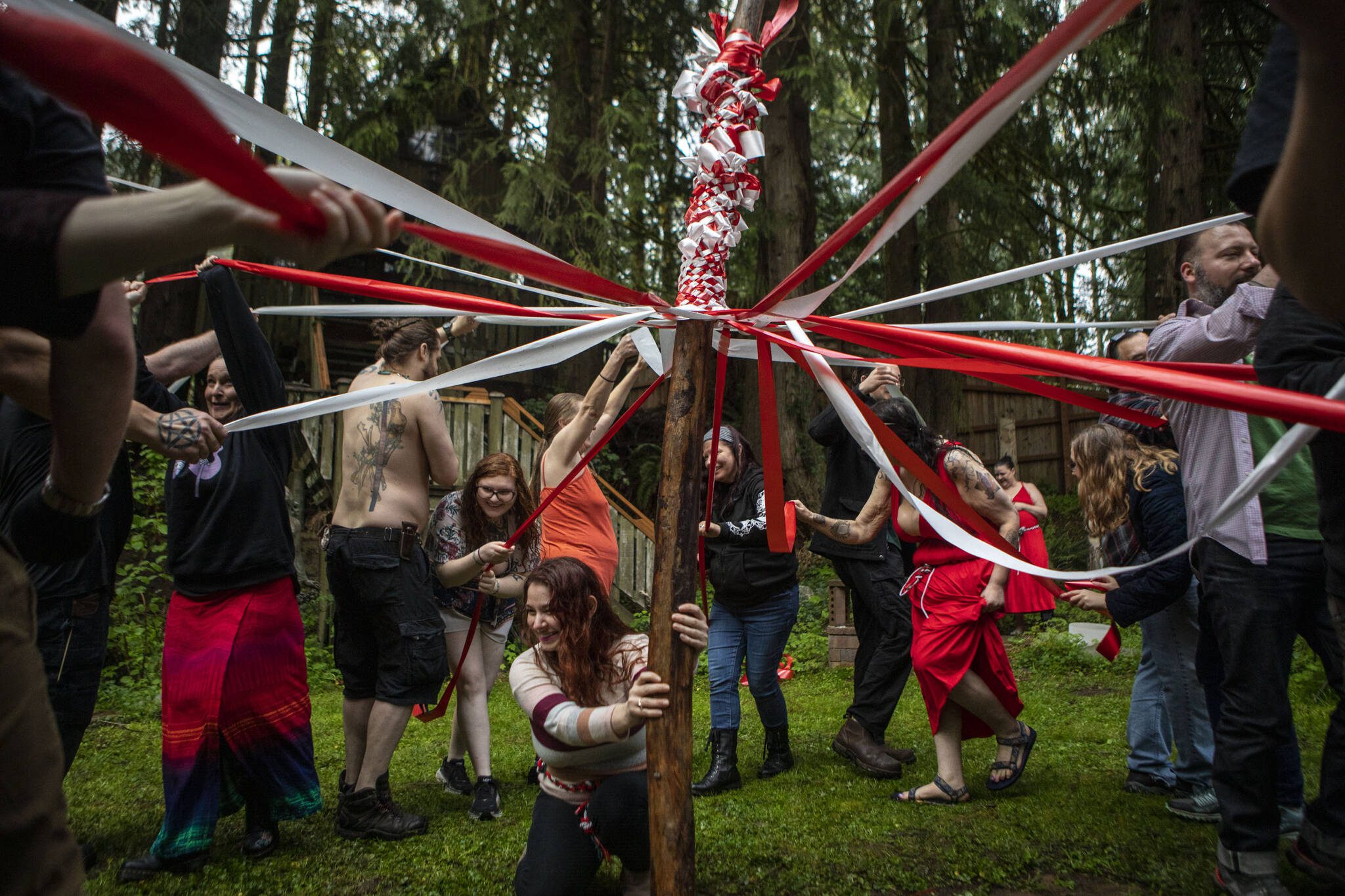 Titania ThunderLily, center, holds the maypole as Pagan revelers wrap red-and-white ribbon around it for a Beltane festival in May 2023, at the Aquarian Tabernacle Church in Index, Washington. Beltane celebrates the height of spring. (Annie Barker / The Herald)