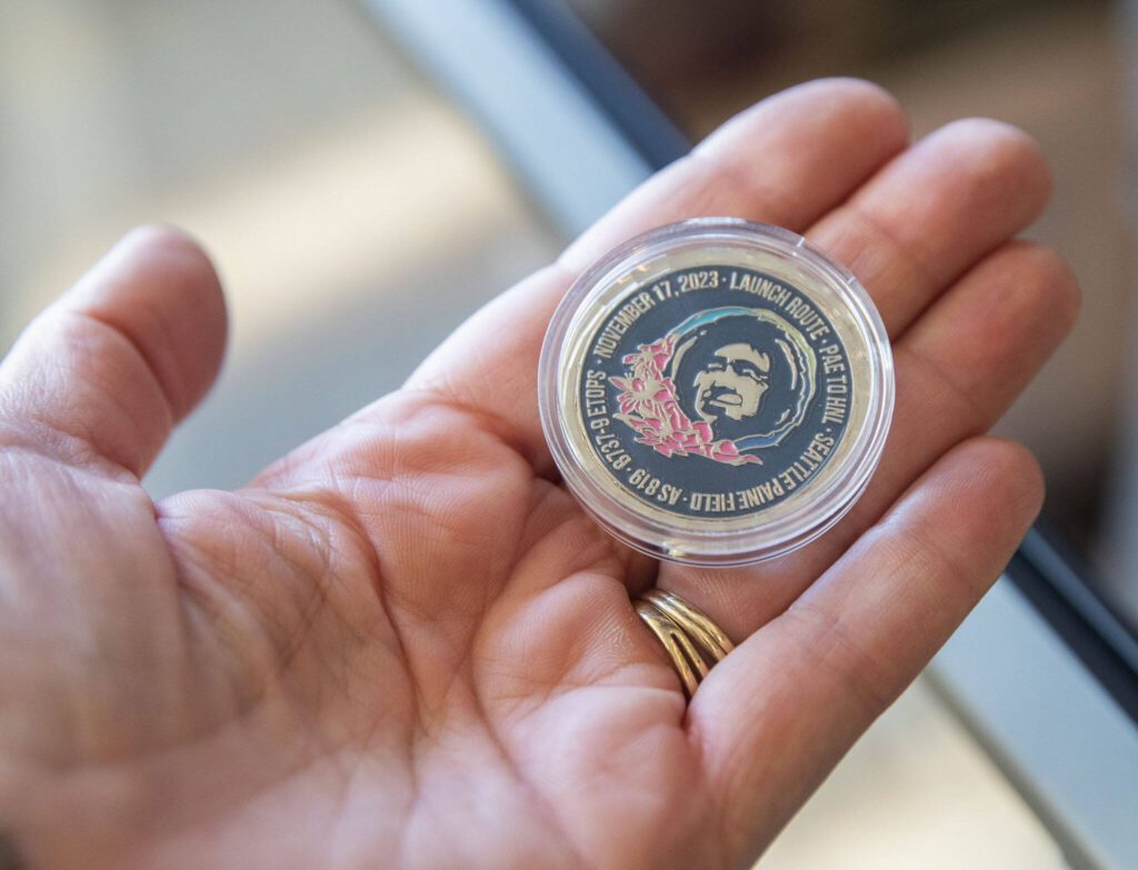 Coins commemorating the first flight from Paine Field to Honolulu are handed out to passengers on Nov. 17, 2023 in Everett, Washington. (Olivia Vanni / The Herald)
