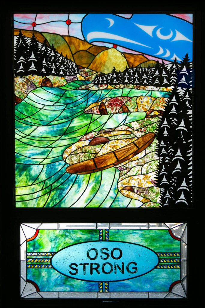 A stained-glass window by local artist James Madison that portrays Steelhead Haven shortly after the slide is seen inside the Oso Fire Department station on Friday, March 15, 2024, in Oso, Washington. (Ryan Berry / The Herald)
